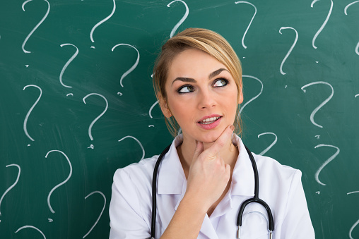 Female Doctor Standing In Front Of Blackboard With Question Mark Signs