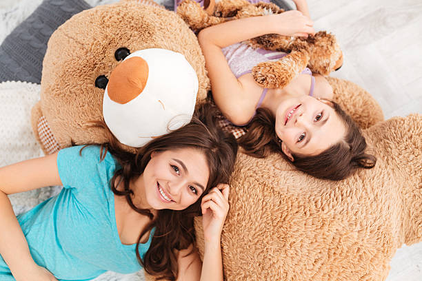 istock Two smiling beautiful sisters lying on big soft plush bear 518470180