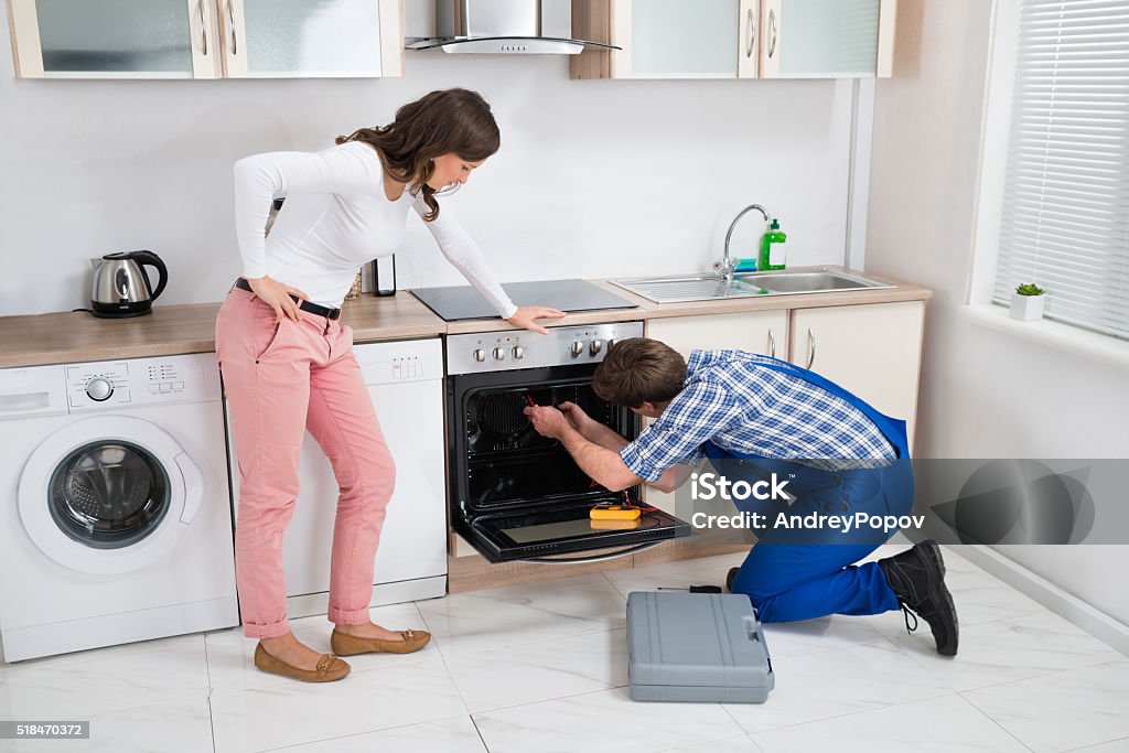 Woman Looking At Worker Repairing Oven Woman Looking At Male Worker Repairing Oven Appliance In Kitchen Room Adult Stock Photo