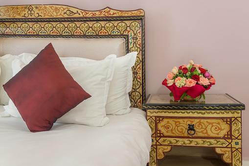 A bouquet of flowers on a bedside table next to a bed with a painted headboard