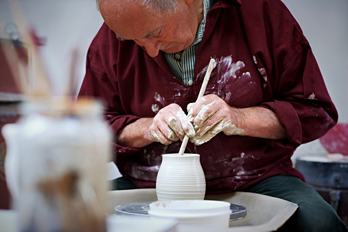 Senior potter shaping pot with tools on pottery wheel