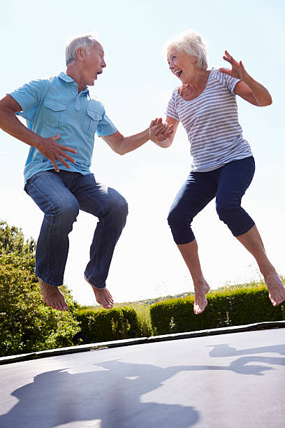 Senior Couple Bouncing On Trampoline In Garden Senior Couple Bouncing On Trampoline In Garden Laughing bouncing photos stock pictures, royalty-free photos & images
