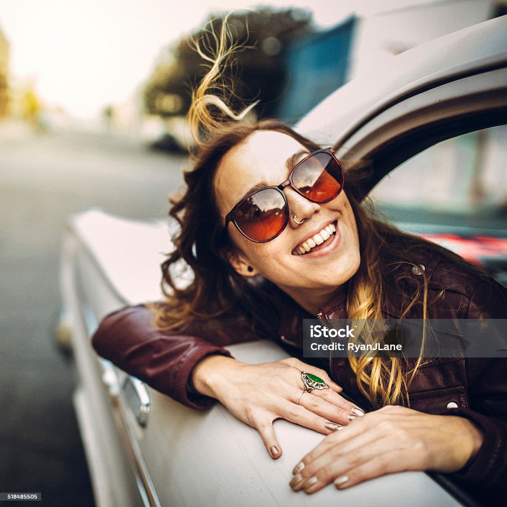 Happy Woman in Classic Car A beautiful smiling young woman leans out the window of a classic car, her hair blowing in the wind and a smile on her face.  Square crop. 20-29 Years Stock Photo