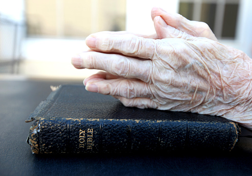 90 year old hand praying over Bible.