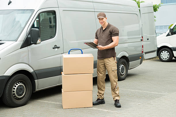 Delivery Man Writing On Clipboard Young Happy Delivery Man With Cardboard Boxes Writing On Clipboard mover delivery person box hand truck stock pictures, royalty-free photos & images