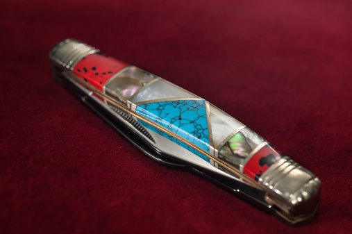 Multi-blade penknife with Native American motives on a burgundy velvety background (selective focus.)