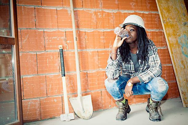 Young builder African woman drinking water at work place