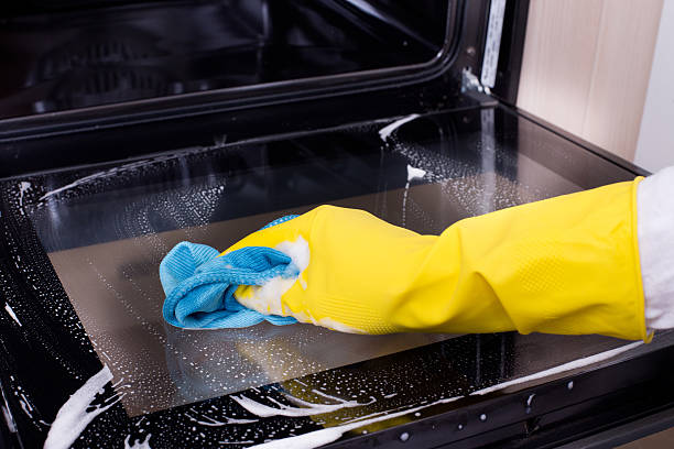 Woman cleaning oven Close up of female hand with yellow protective gloves cleaning oven door oven door stock pictures, royalty-free photos & images