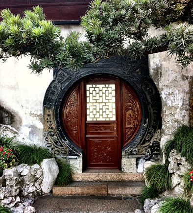 Yuyuan Gardens, Shanghai, China - October 17, 2011: A colour image taken of a circular entrance showing the traditional Chinese attention to detail on the cement archway as well as the decorative solid wood doorway. Solid granite steps and a subtle rock garden balance out and compliment this doorway.