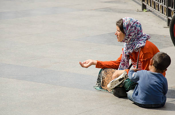 Beggar woman Istanbul, Turkey – September 14, 2014: Begging woman with her child at Eminönü square in Istanbul. While his mother is begging,the child is playing a game in his ow little World. beg alms stock pictures, royalty-free photos & images