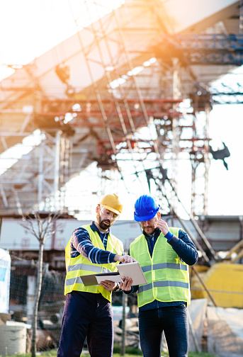 Two experts engineers in protective helmets and fluorescent vests showing the construction site and building activities after the successful project phase. Image taken with Nikon D800 and 85mm developed from RAW in XXXL size, in Novi Sad, Serbia, Central Europe, Europe