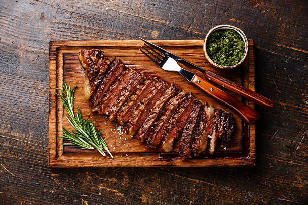 Sliced grilled Striploin steak with chimichurri sauce Sliced grilled beef barbecue Striploin steak with chimichurri sauce on cutting board on dark wooden background chimichurri stock pictures, royalty-free photos & images