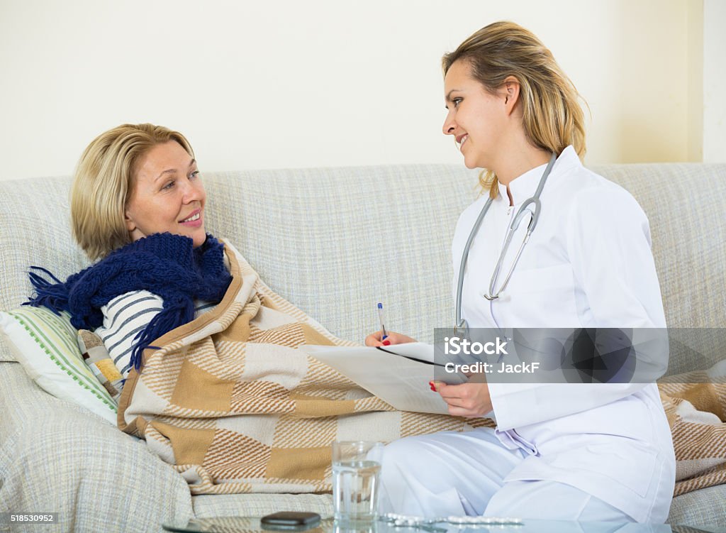 Cheerful doctor helping female pensioner with flue at home Mature woman with flue and fever complaining to senior therapeutist 25-29 Years Stock Photo