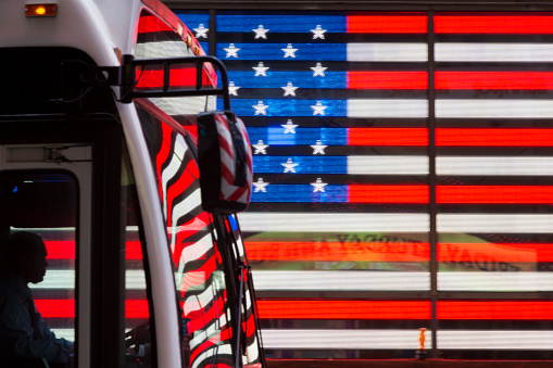 New York, United States - November 22, 2014: Illuminated US flag outside the Times Square Armed Forces Recruiting Station reflected on windshield of the bus at night. Silhouette of a black bus driver is visible against the flag. Midtown Manhattan, Broadway, New York City, USA.