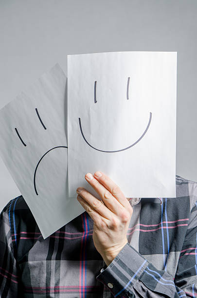 Man holding paper with smiley and sad faces in front of his head, studio shot with grey background