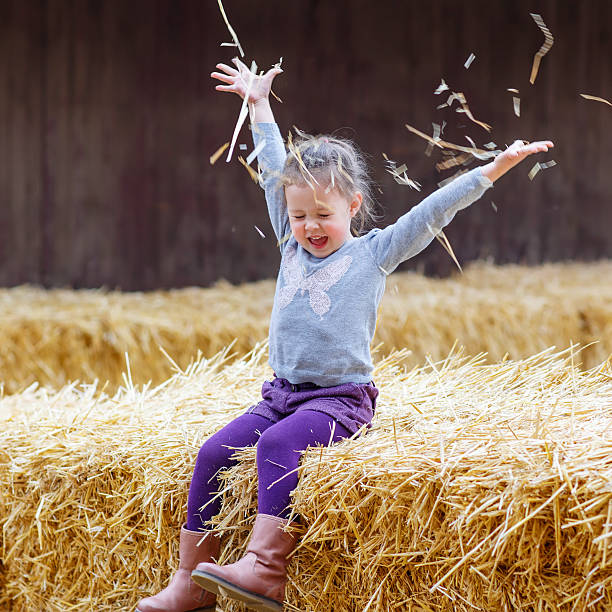 Funny little happy girl having fun with hay on a farm. Child enjoying autumn season and laughing. Happy childhood, lifestyle concept.