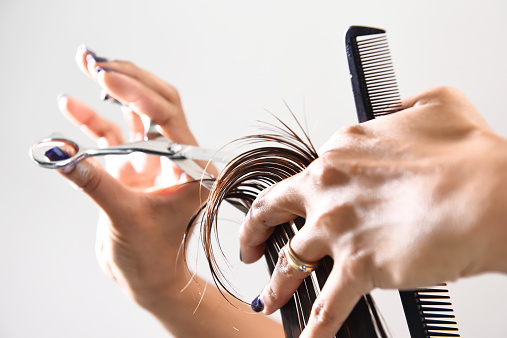 Close up of beautician's hand with a comb cutting hair of woman