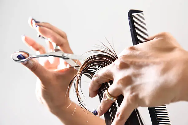 Photo of Hand with a comb cutting hair of woman