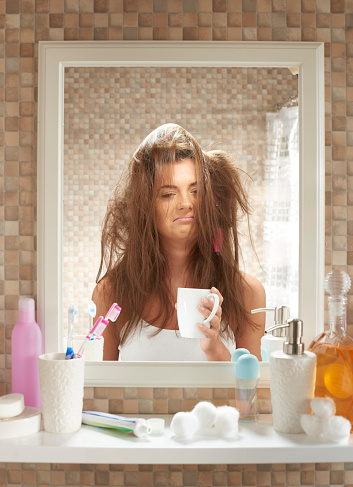 a young woman stands in the bathroom looking in a mirror. She is trying everything to fix her hair but it doesn't seem to be working.