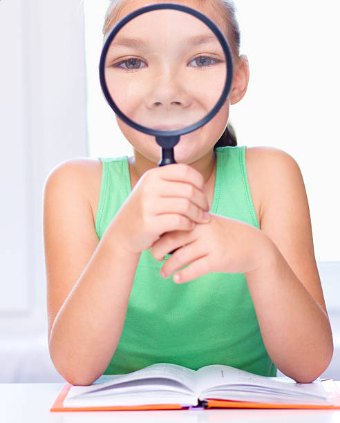istock Girl is looking at big paper using magnifier 518594051