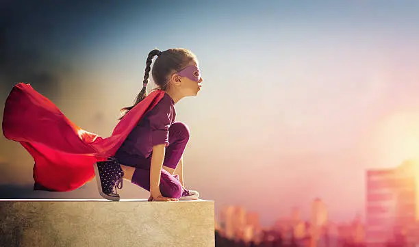 Little child girl plays superhero. Child on the background of sunset sky. Girl power concept