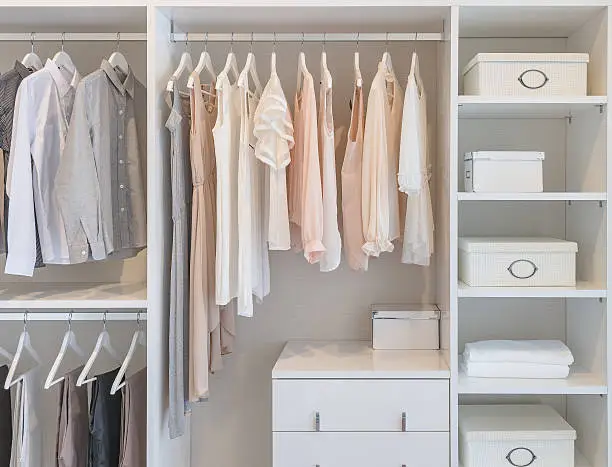 clothes hanging on rail in white wardrobe with boxes