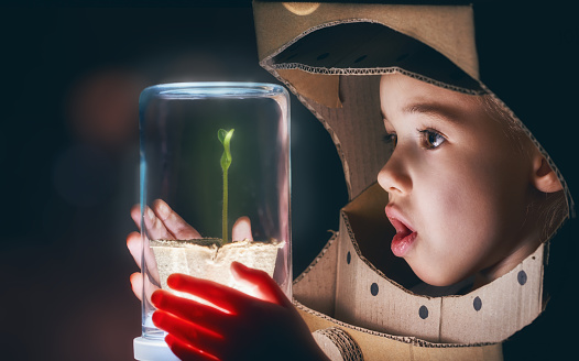 Child is dressed in an astronaut costume. Child sees a sprout in a glass case. The concept of environmental protection.