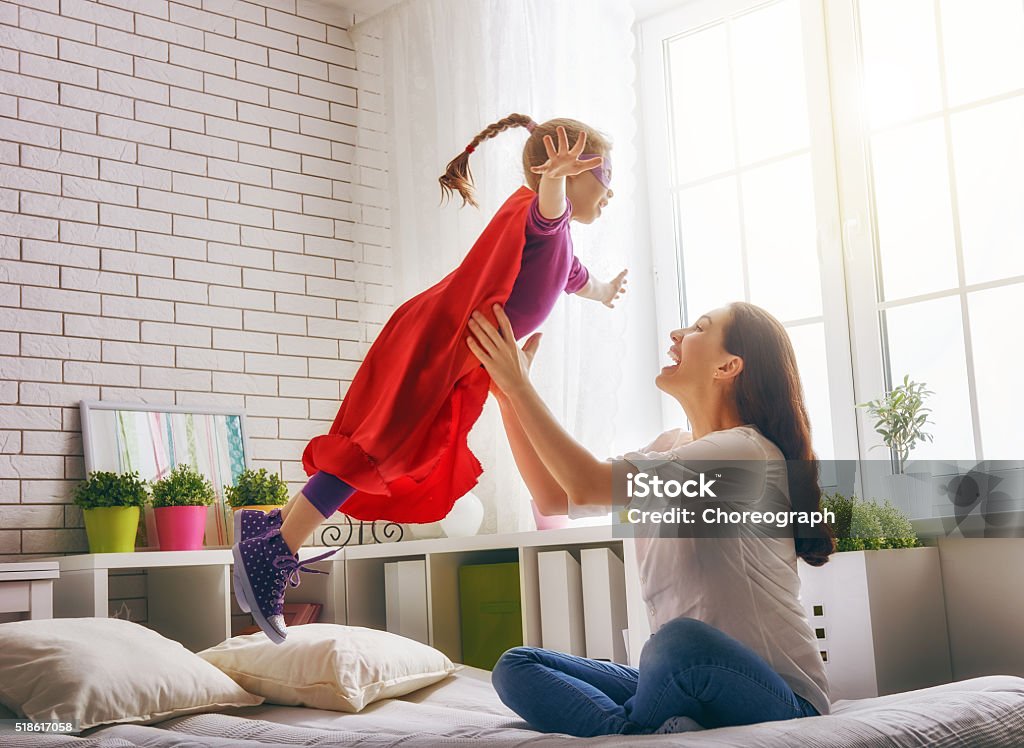 Mother and her child Mother and her child girl playing together. Girl in an Superman's costume. The child having fun and jumping on the bed. Mother Stock Photo