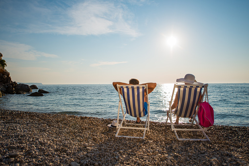 Rear view of mid adult couple sitting on deck chairs at beach during summer. Male and female tourists are at idyllic Vis Island during vacation. They are relaxing on shore at island located in Croatia.