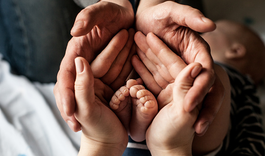 young family of mother of the father and kid. Mother and the father hold legs of the newborn child in the palms.