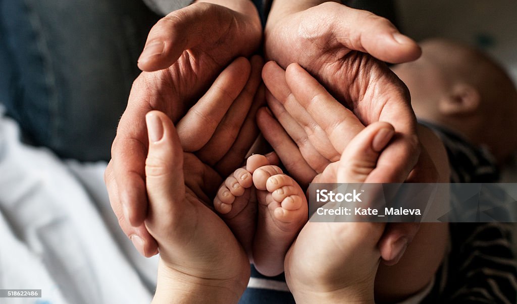 Little child foot in parents palms young family of mother of the father and kid. Mother and the father hold legs of the newborn child in the palms. Family Stock Photo