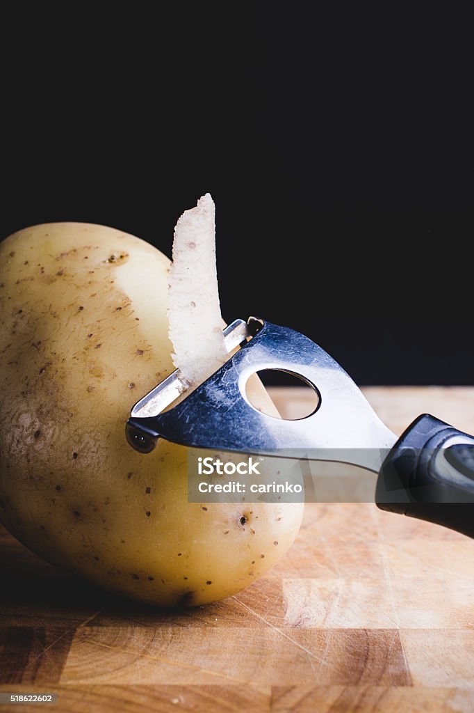 peeling potatoe potatoe peeler and raw potatoe Black Background Stock Photo