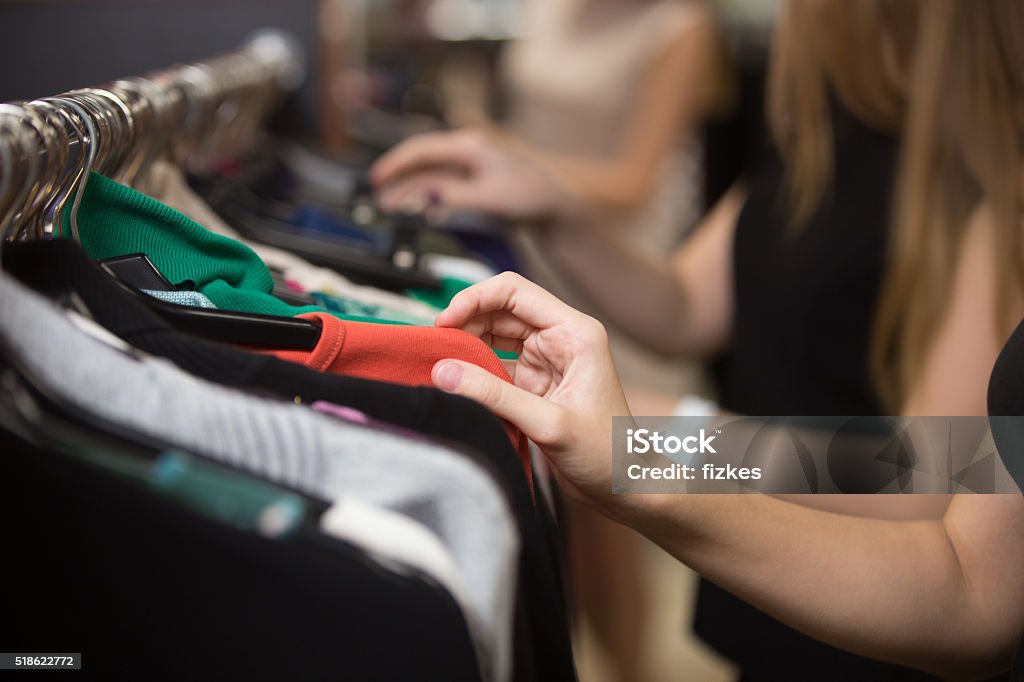 Woman choosing clothes on rack, closeup Young beautiful women shopping in fashion mall, choosing new clothes, looking through hangers with different casual colorful garments on hangers, close up of hands Clothing Stock Photo