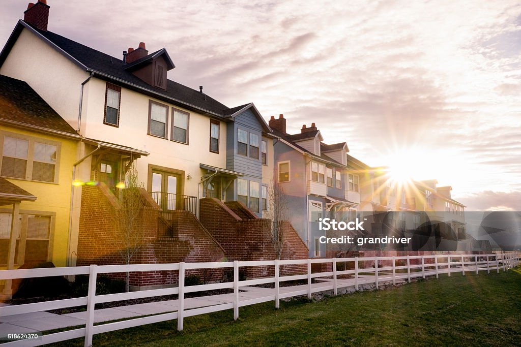 Modern Apartments under a beautiful cloudscape A row of modern apartments under a pretty sunset sky with a white picket fence and vast lawn in front. House Stock Photo