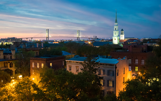 Savannah, Georgia cityscape after sunset with historic buildings, church steeples and suspension bridge.