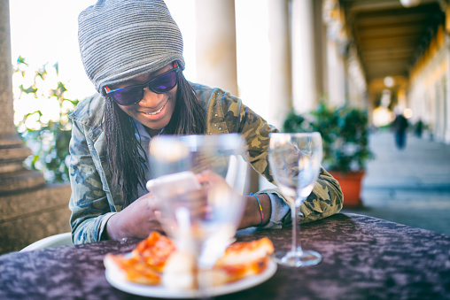 Young African woman messaging in sidewalk cafe, Italy
