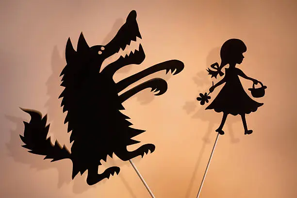 Little Red Riding Hood and the Big Bad Wolf shadow puppets and their shades on the soft glowing screen of shadow theater.