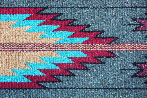 Navajo woven wool rug design. The Navajo stained their yarns for fabrics using natural items from the surroundings - beige from corn silk, tan from brown onion skin, maroon from Juniper bark, amber from Juniper Mistletoe, olive-yellow from sagebrush, gray from Indian Paintbrush, brown from the Gambel Oak, dark green from red onion skin, lavender from Holly berries, dusty orange from canaigre root - just a few of the earthtone colors produced for coloring yarns and other items. Arizona, 2014.