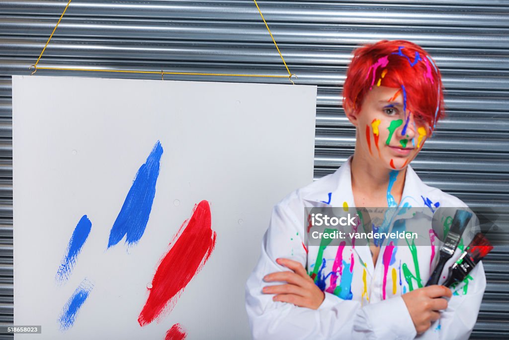 But Is It Art? A pretty redhead stands proudly next to her work of modern art: World Domination in red, white and blue; Part 1. Focus on painting. 20-24 Years Stock Photo