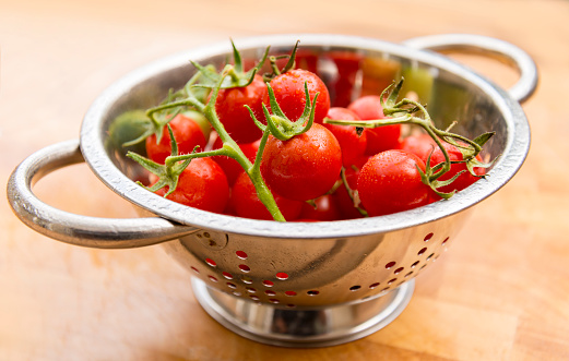 A stainless steel collander holds a stack of juicy, red, vine-ripened cherry tomatoes