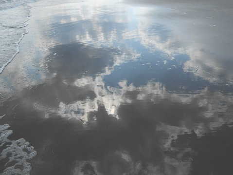 Clouds and Sun Reflecting in Wet Sand from Rolling Waves on Coney Island Beach in Brooklyn, New York, NY in Summer.