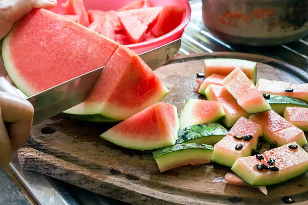 A juicy watermelon is being cut on a wooden cutting plate with a metallic knife