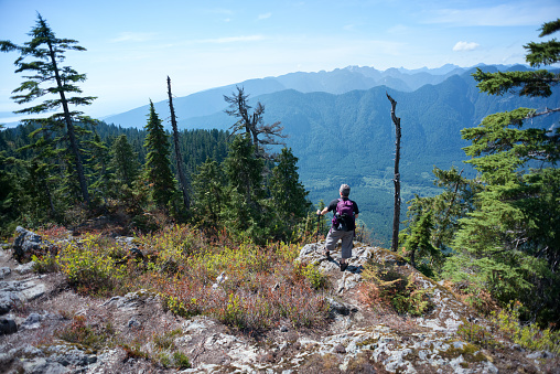 A mature male backpacker stands on a mountaintop and enjoys the view.  Mount Seymour, North Vancouver, British Columbia, Canada.  View of the valley and surrounding mountains in the background.