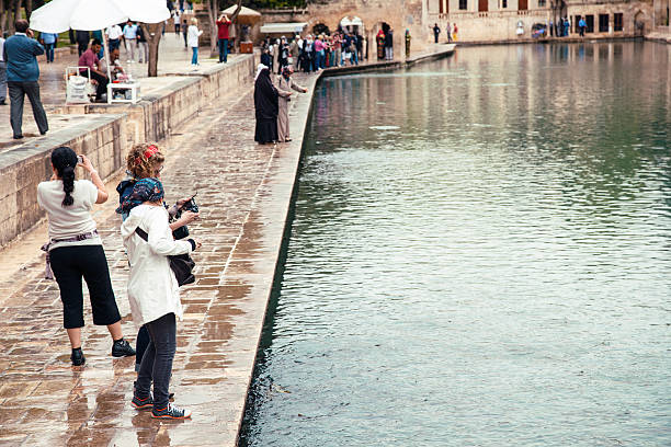 Sanliurfa, Turkey - May 10, 2012: People walking around the Sacred Fish Lake and Halil Rahman Mosque in the center of Sanliurfa.This is the place where according to legend the prophet Abraham was thrown into a fire, but by a miracle the fire turned into a pool. The legend says wood from the fire turned into fish.