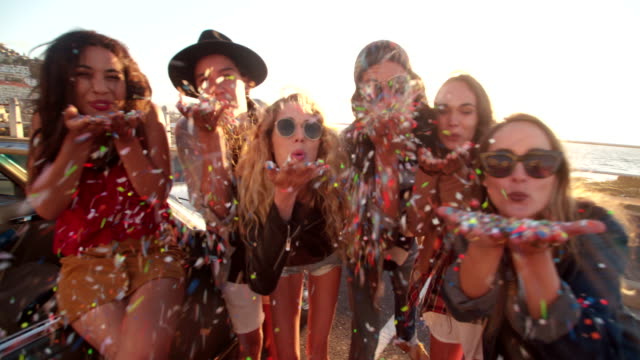 Teenager hipster friends celebrating by blowing colorful confetti from hands