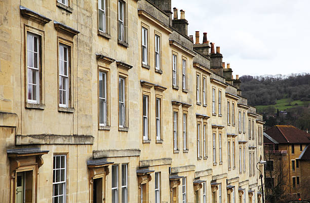 Sunlight in a cloudy blue sky frames the symmetrical angles of the towering Georgian sculptured architectural  facade on this low angle view of this balconied block of terraced houses, living accommodation building in Clifton, Bristol, England, UK