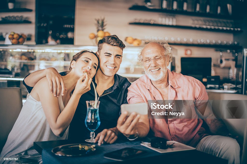 Senior man using digital tablet with teenage couple Cocktail Stock Photo