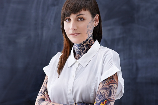 A cropped studio shot of a young professional with tattoos on her neck and arms