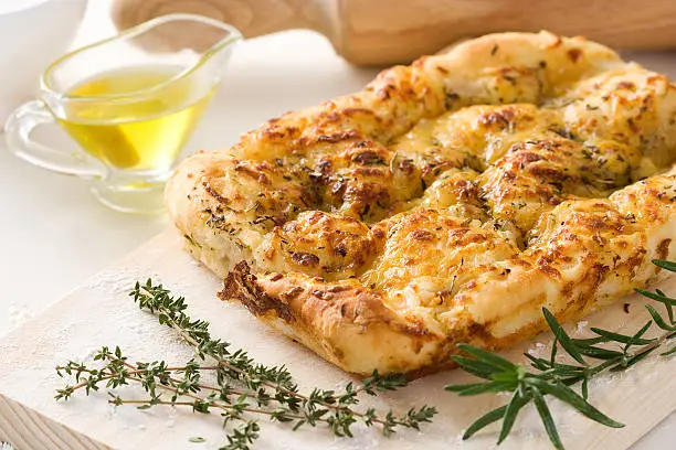 Italian focaccia bread with oregano, olive oil and rosemary on a cutting board.