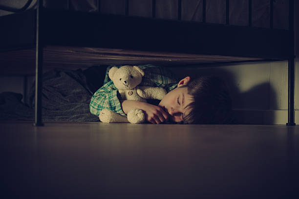 Scared Boy Sleeping Under his Bed with Teddy Bear Scared Young Boy Sleeping Under his Bed Inside his Room While Hugging his Teddy Bear Stuffed Toy at Night. man with teddy bear stock pictures, royalty-free photos & images